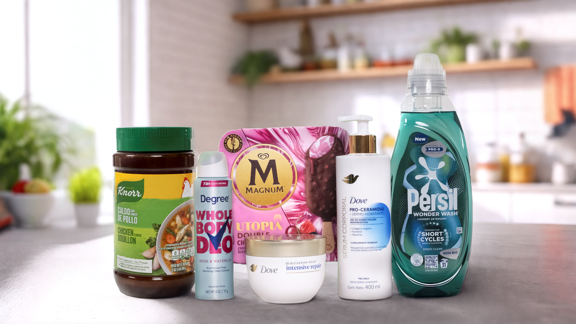A Unilever különböző Power Brand márkái elrendezve egy konyhapulton. Balról jobbra haladva látható egy Knorr csirkehúsleves-kocka üveg, egy Degree dezodor spray a "WHOLE BODY DEO" felirattal, egy "UTOPIA" feliratú Magnum jégkrém doboz, egy Dove testápoló pro-ceramid szérummal, egy Dove Intensive Repair krém üveg és egy Persil Wonder Wash mosószer flakon. A háttérben egy modern konyha látható növényekkel és különféle tárgyakkal a polcokon.